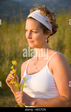 Il 30-anno-vecchia donna azienda fiori e guardare il tramonto su un pendio erboso, Santa Barbara, California Foto Stock