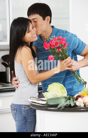 Uomo asiatico kissing ragazza e dando i suoi fiori in cucina Foto Stock