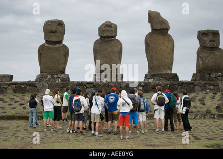 Turisti si riuniscono di fronte alla pietra scolpita nelle figure, o il moai, a Ahu Tahai vicino a Hanga Roa sull'Isola di Pasqua. Foto Stock