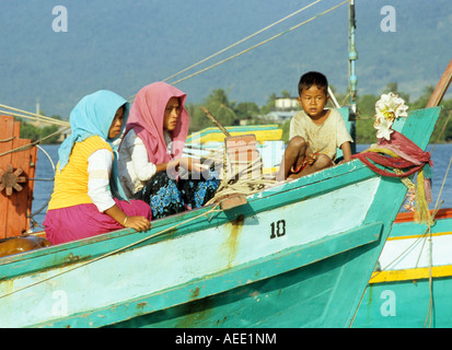 Due musulmani Cham donne e un giovane ragazzo seduto su una barca da pesca sul fiume Sanke, Kampot, Cambogia Foto Stock