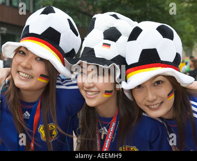 Tre femminili giapponese i tifosi di calcio in buon umore in posa con cappelli e adesivi in tedesco colori nazionali Foto Stock