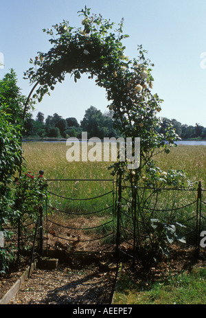 Ferro da stiro garden gate great barton Suffolk England Regno Unito vista attraverso le rose coperta arco sul prato verso il lago Foto Stock