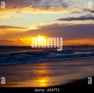 Impostazione di sole su di un terreno non lavorato con onde che si infrangono sulla spiaggia Foto Stock