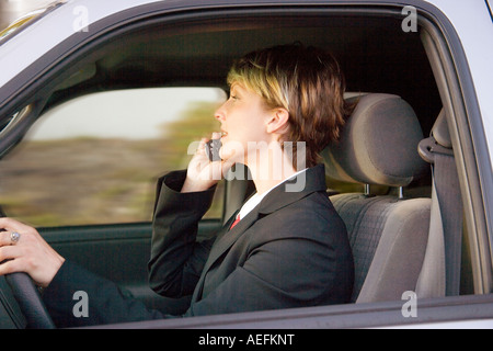 Azienda giovane donna alla guida di una vettura ed a parlare su un telefono cellulare Foto Stock