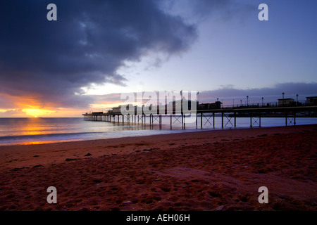 Alba sul foreshore a Paignton Devon meridionale con il molo vittoriano in background e il sorgere del sole in un cielo nuvoloso Foto Stock