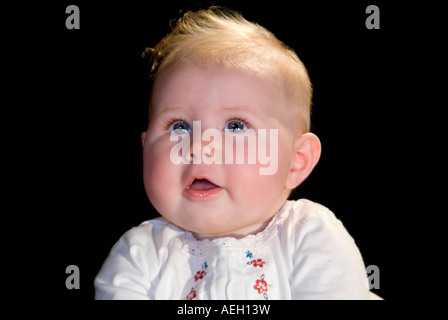 Chiudere orizzontale su ritratto di un periodo di sei mesi di età caucasian Baby girl in posa per fotografie contro uno sfondo nero Foto Stock