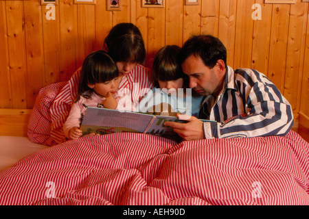 Famiglia la lettura di un libro per bambini in letto. Foto di Willy Matheisl Foto Stock