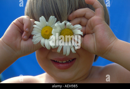 Bambino con marguerites tenendo le mani davanti agli occhi. Foto di Willy Matheisl Foto Stock