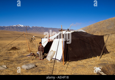 Il Nomad ragazzo al di fuori di yak-capelli tenda con le montagne alle spalle sulle praterie Sangke vicino a Xiahe, Gansu, Cina Foto Stock