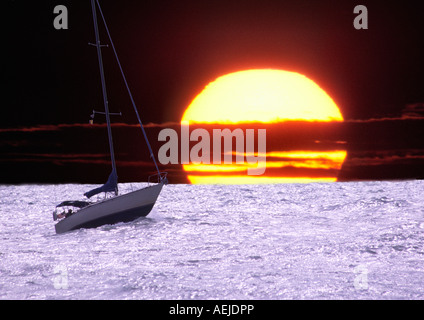 Nave a vela o barca a vela su un oceano e un enorme sole che tramonta dietro Foto Stock