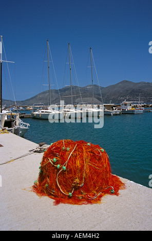 Pila di rosso e arancio reti da pesca sul Quayside e yachts, Lixouri Harbour, Lixouri, Cefalonia, Grecia Foto Stock