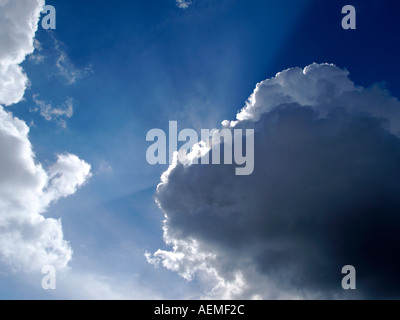 La luce del sole dietro il Cumulus nuvole con raggi di luce CRESPULAR contro un profondo cielo blu Foto Stock