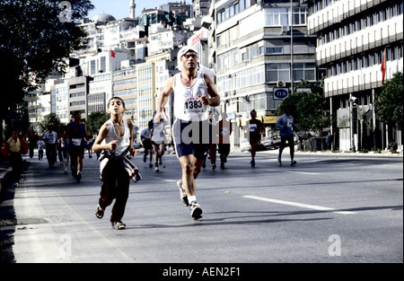 Ragazzo che corre ufficiosamente nella maratona di Istanbul, indossando sandali con un corridore adulto al suo fianco Foto Stock
