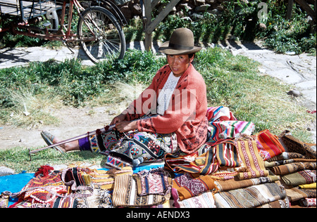 Donna tessitura e seduto accanto a tessuti tradizionali doni, Pisac Market, Pisac, vicino a Cusco, Perù Foto Stock