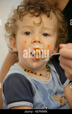 Kleinkind 18 Monate alt JONI mit Bernsteinkette um den Hals beim Essen mit verschmiertem Gesicht Modello rilasciato Foto Stock