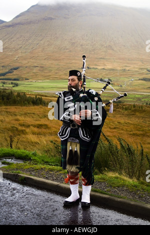 Piper in highland dress giocando sul ciglio della strada vicino a Bridge of Orchy Foto Stock