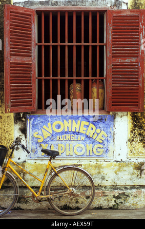 Vecchio weathered Savonnerie Xuong Lam Xa Phong segno, persiane alle finestre e giallo bicicletta, ad Hoi An, Viet Nam Foto Stock