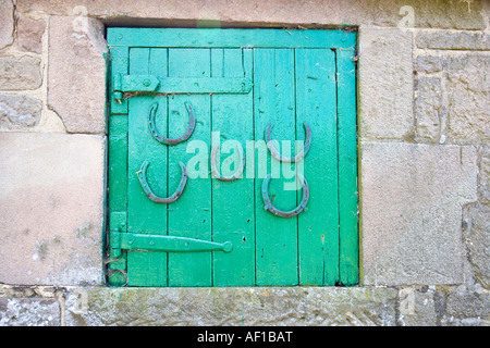 Di legno verniciato di fieno porta Loft impostato in un muro di pietra con cinque ferri di cavallo attaccato Foto Stock