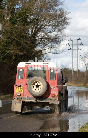 Land Rover Defender auto guidando lungo una strada allagata in Inghilterra rurale Foto Stock