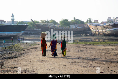 Le donne indiane che trasportano il loro shopping sulle loro teste attraverso il cantiere navale di legno, Mandvi, Kutch, Gujarat, India Foto Stock