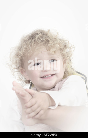 Bambino in una scuola materna a sorridere mentre tiene il suo piede in un modo carino Foto Stock