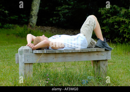 Ragazzo adolescente tenendo nap sulla panca in legno nel parco Foto Stock