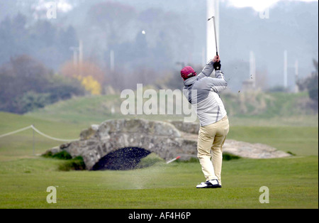 Il golfer prendendo un colpo al di sopra del ponte Swilcan sul vecchio corso St Andrews in Scozia Foto Stock