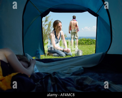 Vista attraverso l'apertura della tenda con giovani donne dormire dentro mentre un altro cuochi fuori con un giovane maschio in piedi Foto Stock