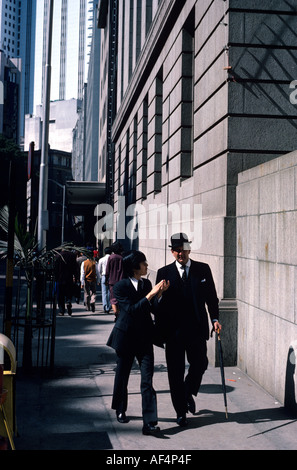 Città inglese gent nel cappello bowler fine degli anni settanta a piedi con uomo cinese sia in abiti nel quartiere centrale di strada di Hong Kong Foto Stock