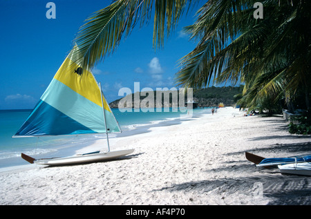 Piccola barca a vela con giallo e bianco blu verde vela sulla spiaggia di sabbia bianca al Dickinson Bay Antigua Caraibi Foto Stock