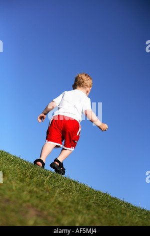 Bimbo di 2 anni a piedi dalla fotocamera su erba con un luminoso cielo blu. Foto Stock