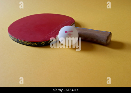 Table Tennis bat in appoggio su un tavolo da ping pong palla su uno sfondo giallo Foto Stock