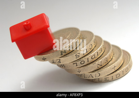 Una casa monolopy seduti sulla sommità di una pila o pile di monete per illustrare la variazione dei tassi di interesse e i prezzi delle abitazioni. Foto Stock