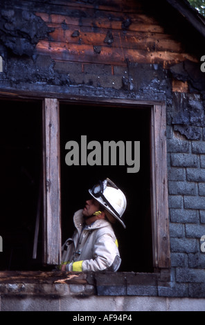 Un incendio fighter indagando il fuoco delle prove in un bruciato sul telaio di una finestra della struttura bruciato Foto Stock