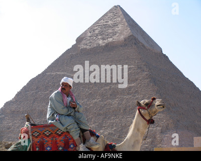 Fumatori uomo egiziano seduto su un cammello di fronte di una Piramide di Giza in Egitto, Kairo, Giza, Gizeh, Giseh Foto Stock