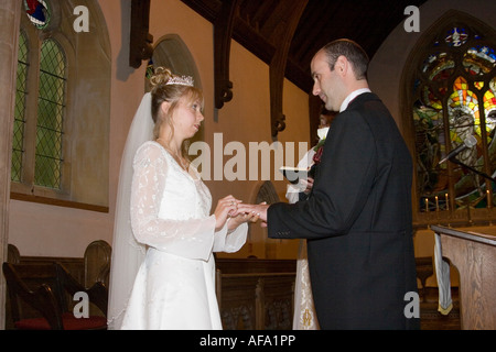 Paio di stare faccia a faccia lo scambio di anelli durante un cristiano cerimonia di matrimonio in una chiesa di Norfolk Foto Stock