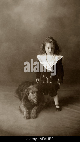 Studio ritratto di un ragazzo edoardiano con un cane da compagnia che indossa una tuta alla moda di tipo 'Little Lord Fauntleroy' con un grande colletto in pizzo, circa 1910, Regno Unito Foto Stock