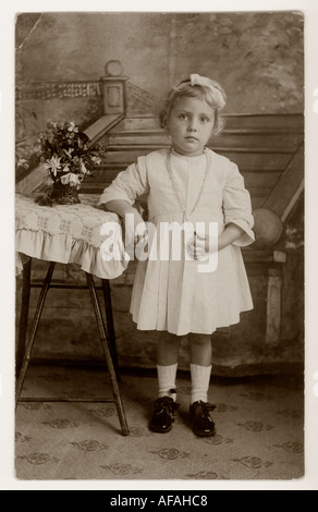 Innocente giovane ragazza che guarda dolce in primo vestito di comunione Santa che tiene un crocifisso nel 1918 Foto Stock