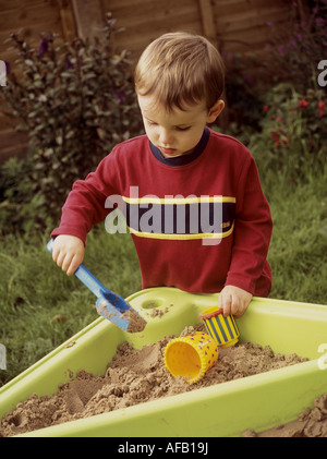 Giovane ragazzo giocando con una forcella di plastica e contenitori in un vassoio di sabbia Foto Stock