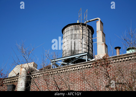 Un arrugginito serbatoio acqua sulla parte superiore di un edificio in mattoni contro un cielo blu Foto Stock