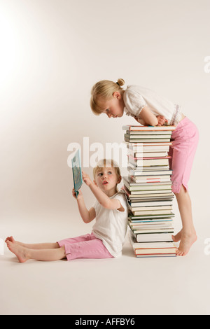 Due ragazze seduto su una pila di libri lettura insieme Foto Stock