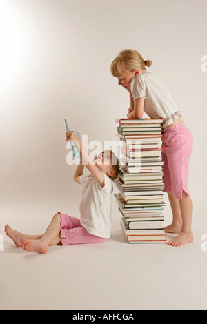 Due ragazze guardando libri la lettura di due ragazze seduto su una pila di libri lettura insieme Foto Stock