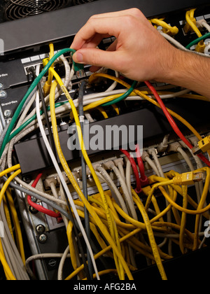 Un paio di router in un armadio di patch con i lotti e lotti di cavi nel groviglio e una mano di collegare un filo Foto Stock