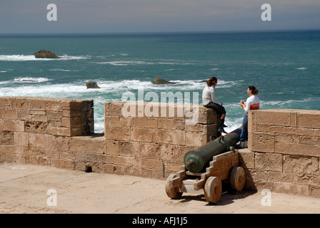 Due persone che guardano con vista sul mare da vecchi bastioni Skala de la Ville Essaouira costa atlantica del Marocco del Nord Africa Foto Stock