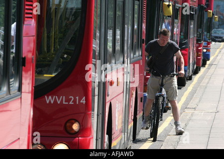 Un ciclista tesse tra gli autobus in London REGNO UNITO Foto Stock