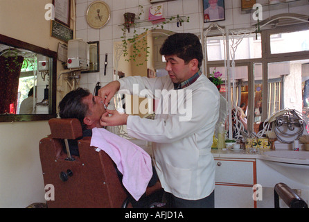 Barbiere il taglio di capelli e la rasatura di un uomo nel piccolo negozio nella città di Mulga nel sud-ovest della Turchia. Foto Stock