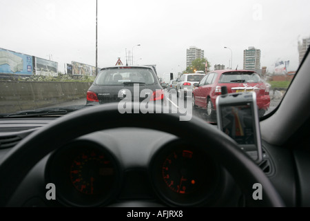 Cruscotto e volante della vettura bloccato nel traffico di utilizzo di PDA sat nav sul giorno di pioggia su dal Westlink Foto Stock