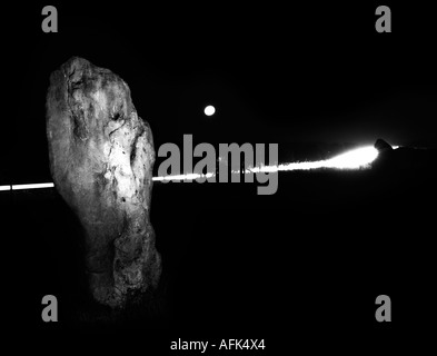 Parte di West Kennet Avenue (Avebury) illuminata di notte con la luna piena e faro auto trail in background. Wiltshire, Inghilterra, Regno Unito. Foto Stock