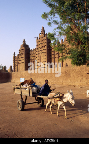 Un ragazzo aziona il suo asino carrello passato la Grande Moschea di Djenne. Il Sahel moschea di stile è il più grande del mondo di mattoni di fango struttura. Foto Stock