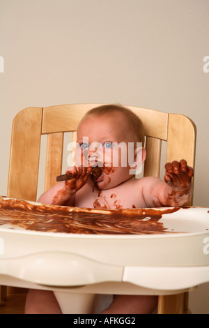 Il bambino nel seggiolone rendendo pasticcio con budino di cioccolato Foto Stock